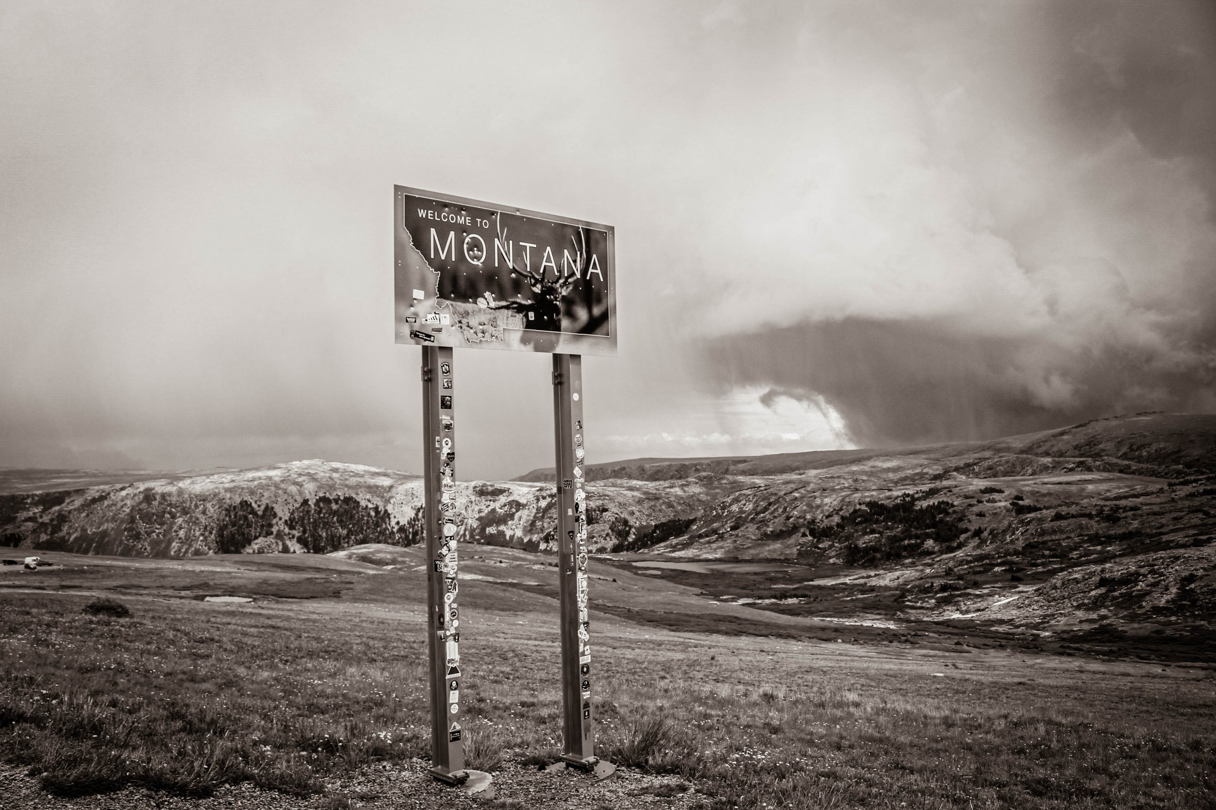 Welcome to Montana sign with scenic mountainous landscape in background, under cloudy skies