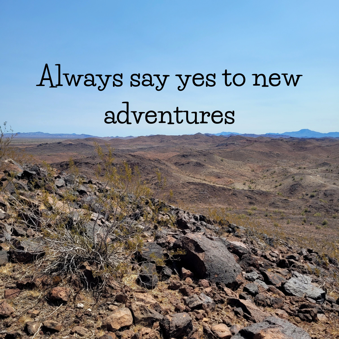 Desert landscape with rocks and sparse vegetation under blue sky, featuring the text 'Always say yes to new adventures.'