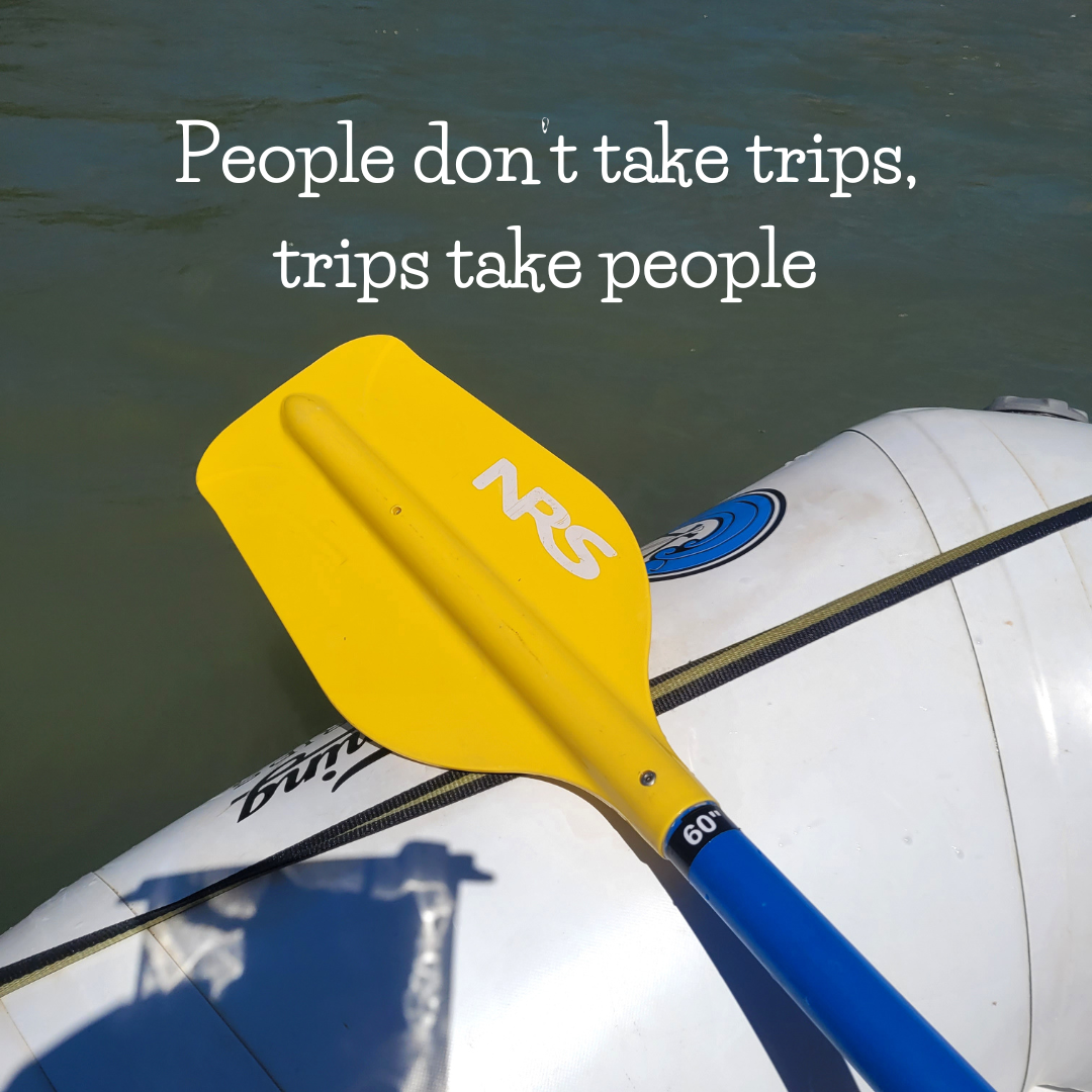 Yellow paddle labeled "NRS" on an inflatable raft with water in the background and the text "People don't take trips, trips take people."