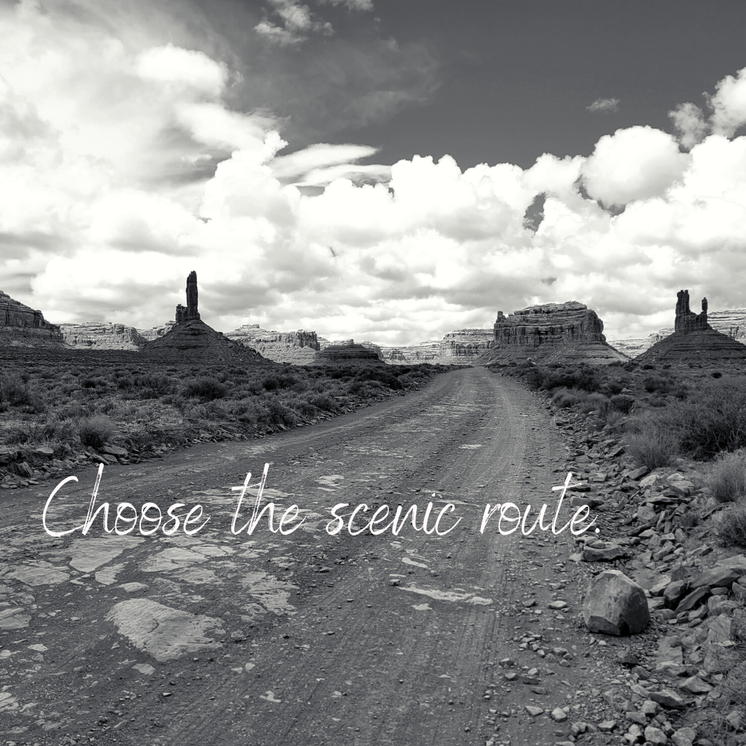 Desert landscape with dirt road, rock formations, and cloudy sky, text "Choose the scenic route" in foreground.