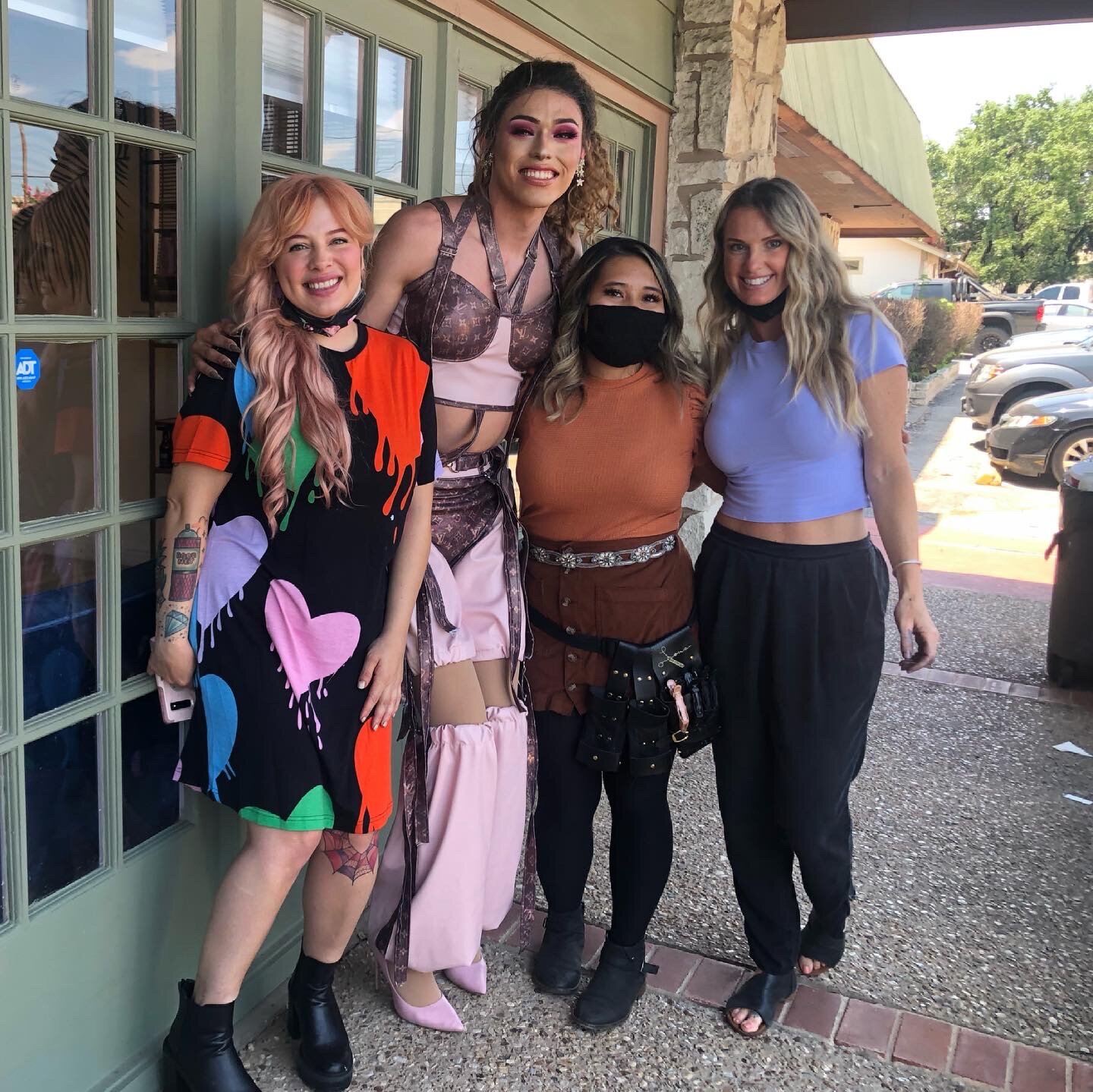 Five women standing outside a building, smiling at the camera. They are dressed casually and some are wearing face masks.