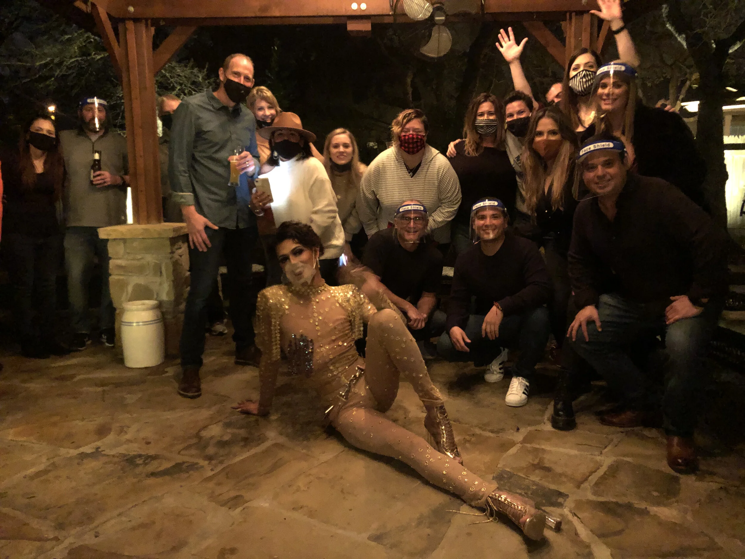 A group of people, including a performer in a gold costume, posing together at a social gathering outdoors at night.