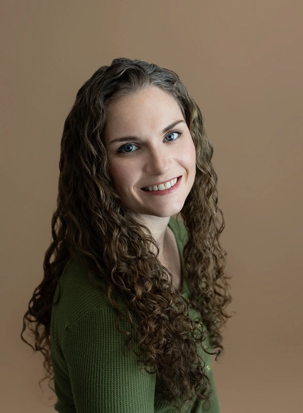 woman with brown, curly hair, blue eyes, and green shirt