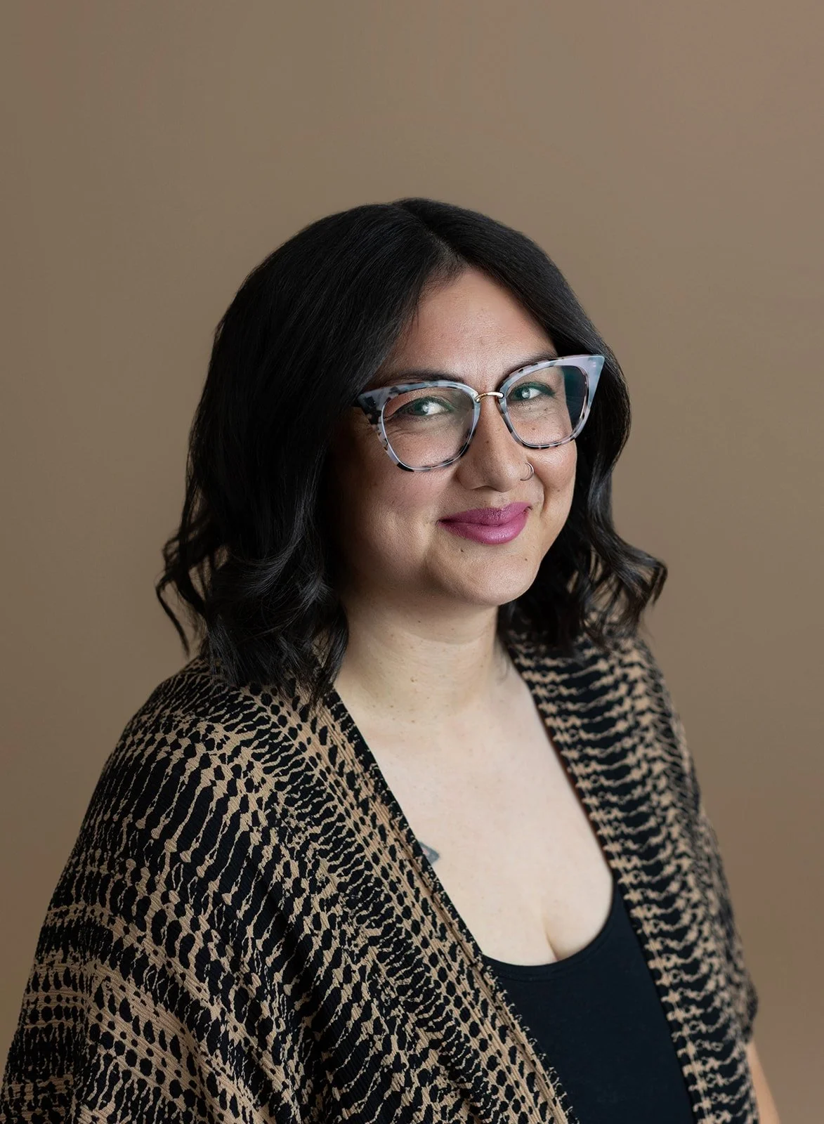 woman with dark hair, thick-framed glasses, and pink lipstick