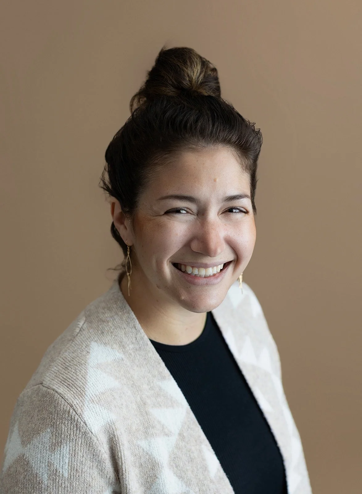 smiling woman with brown bun, black shirt, and tan cardigan