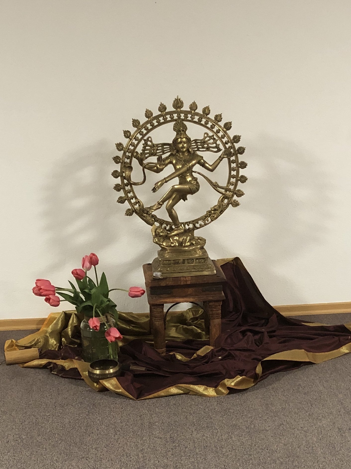 Bronzefigur des hinduistischen Gottes Shiva, auf einem kleinen Holzstuhl, mit Blumen und Stoff dekoriert.