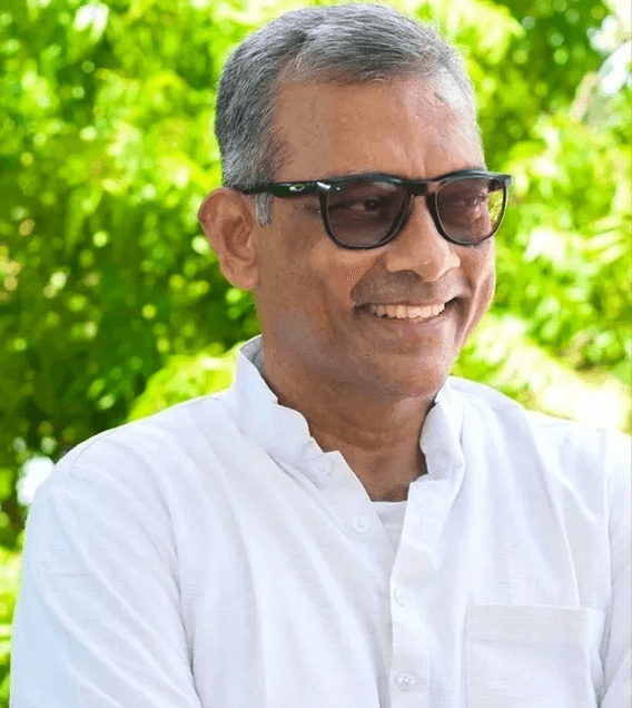 Ravi Shankar, dunklen Sonnenbrillen und weißem Hemd vor einem grünen Baum.