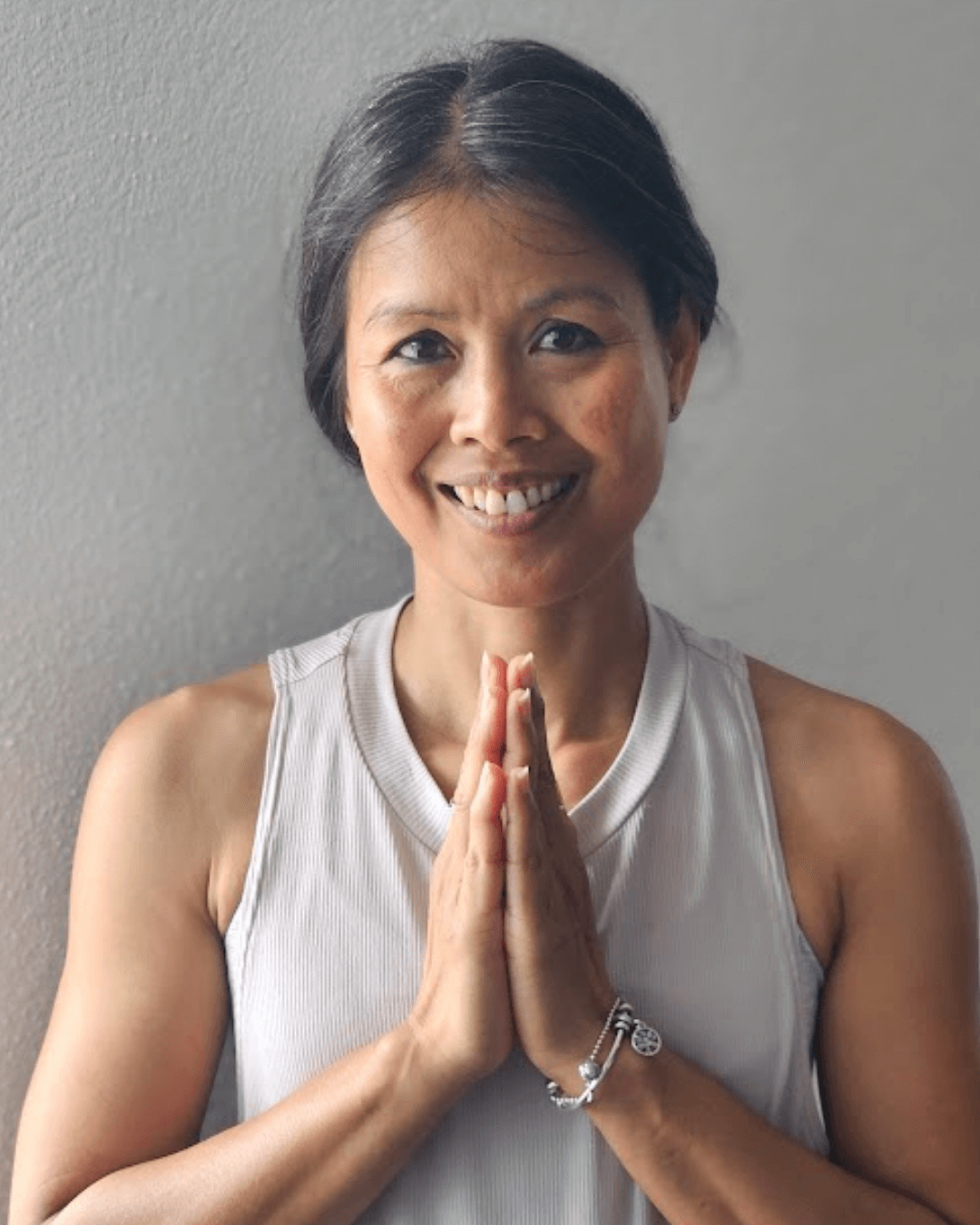 Wisa Schmitt, in einer weißen ärmellosen Sporttop, die ihre Hände in einer Gebetsposition vor ihrer Brust hält, vor einer hellgrauen Wand.