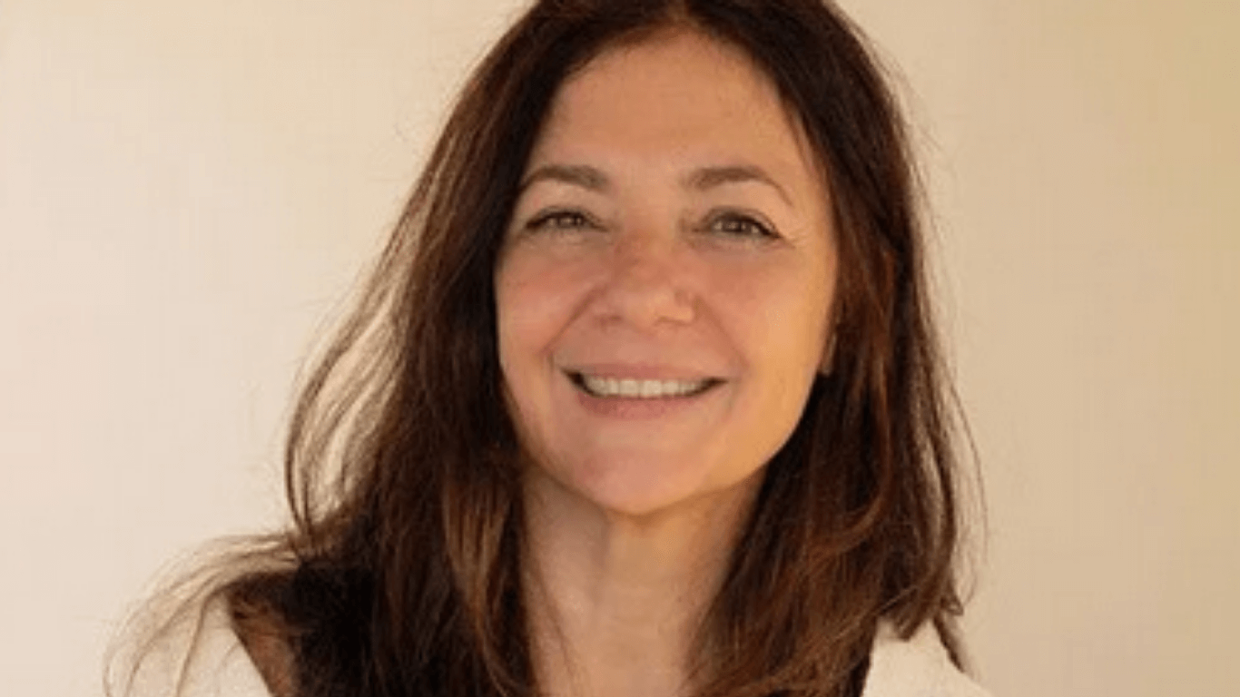 Ein Porträt von Laura mit braunen, lockigen Haaren gegen einen hellen Hintergrund.