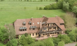 Großes Haus auf einem grünen Grundstück mit Bäumen, mehrere Dachgauben und Balkone