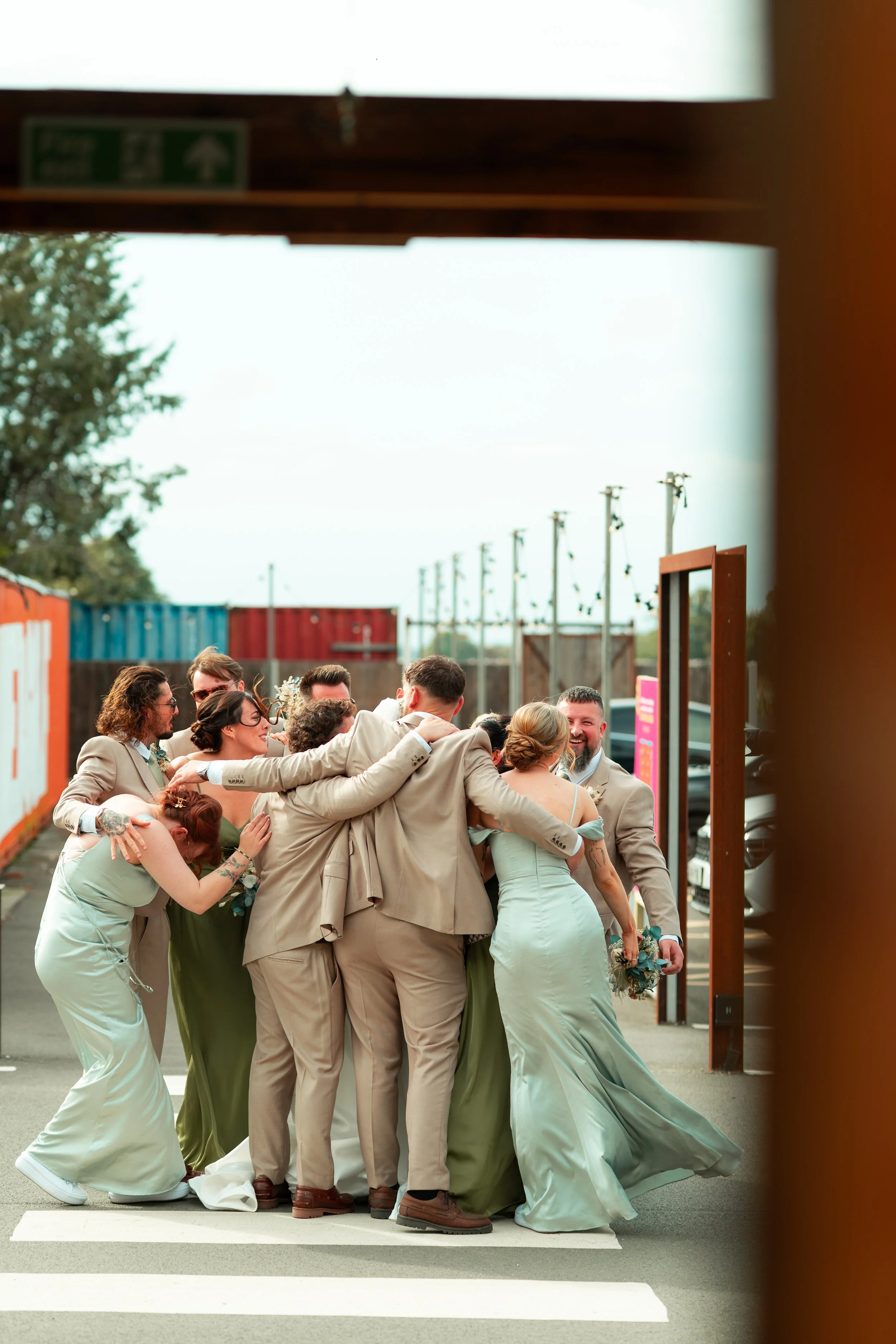 A group of people dressed in wedding attire hugging and celebrating outdoors.