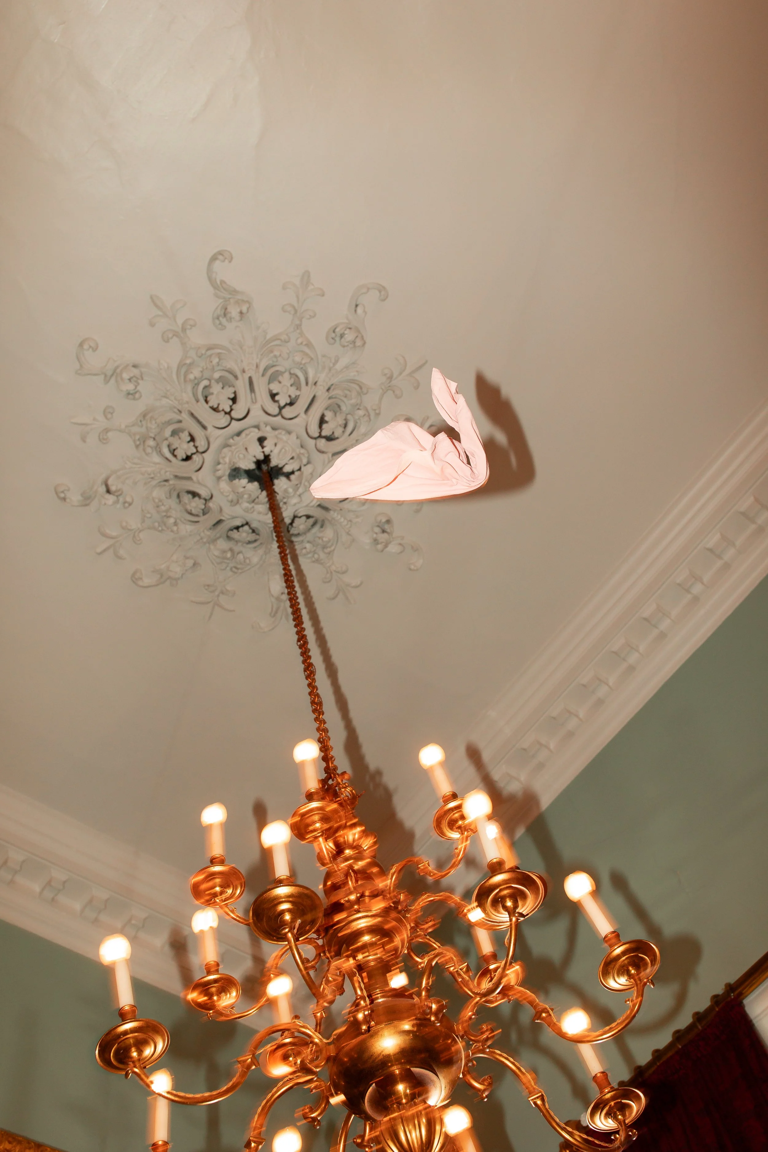 A ceiling with an ornate decorative medallion, chandeliers, and a paper crane hanging from a chain.