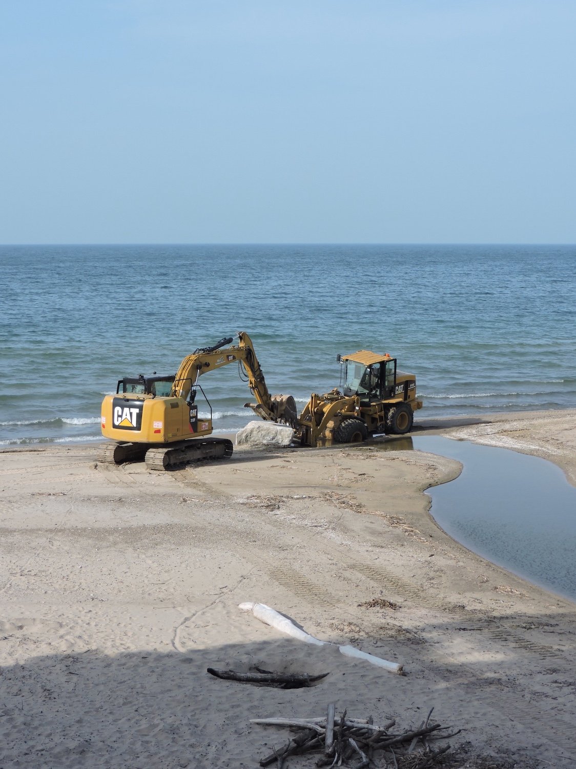 Each boulder came down the beach on a front end loader to get stuck in the drain and picked up by the tracked backhoe.