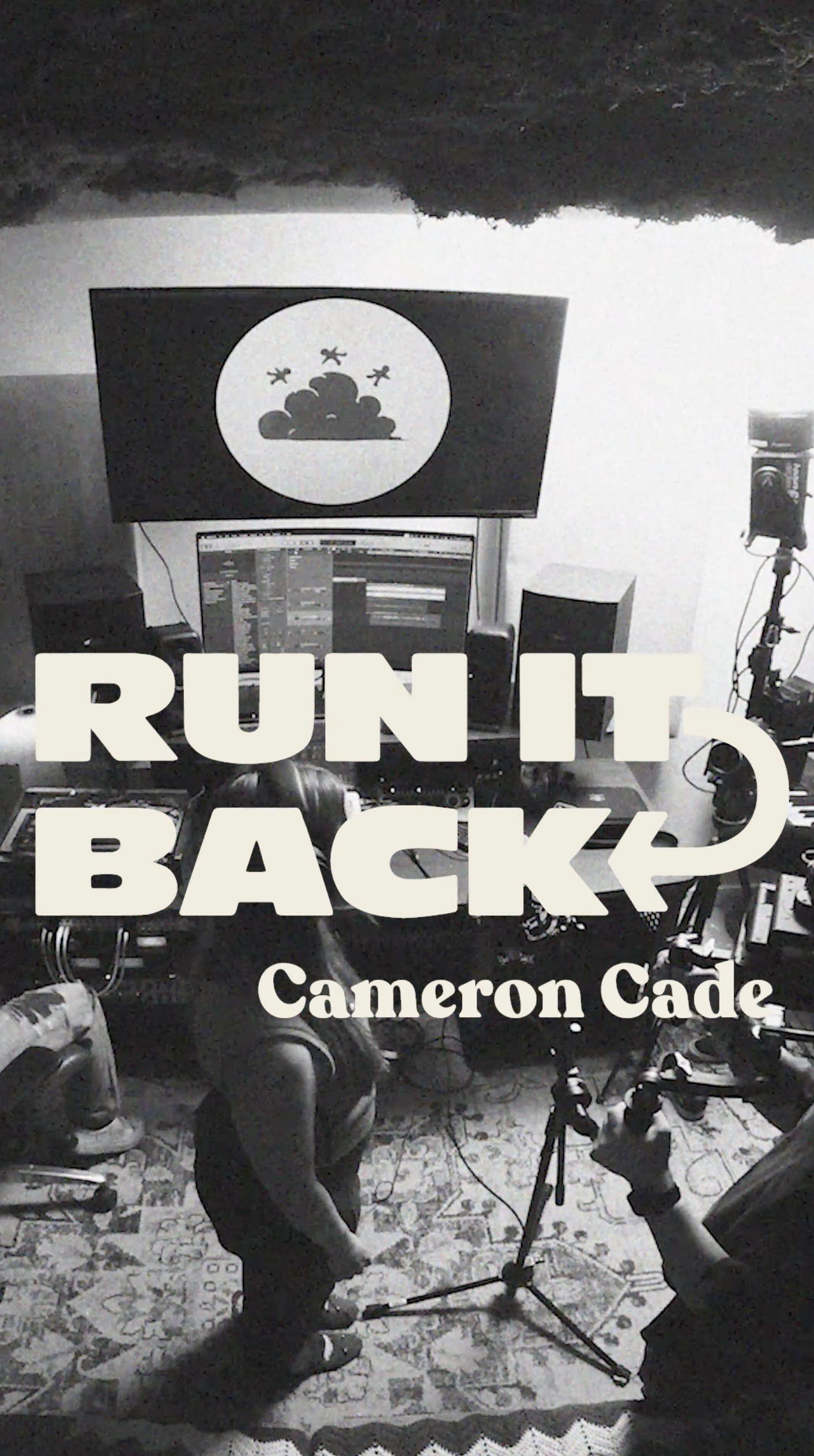 Black and white photo of a music studio with electronic equipment, two people, and a large screen displaying a cloud and birds. Text overlay reads 'Run It Back' and 'Cameron Cade'.