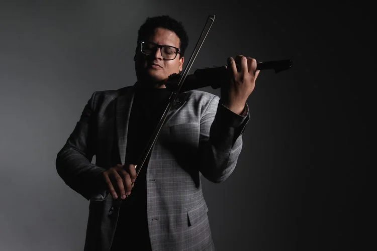 Person playing a violin in a dimly lit setting with a dark background.
