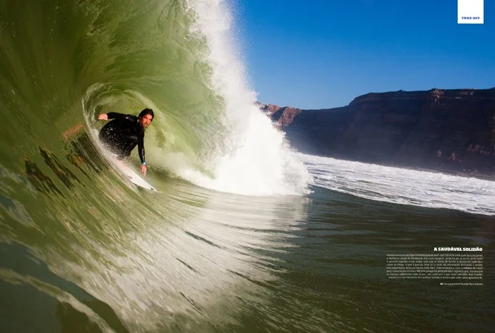 A person surfing inside a large green wave near a coastline with cliffs.
