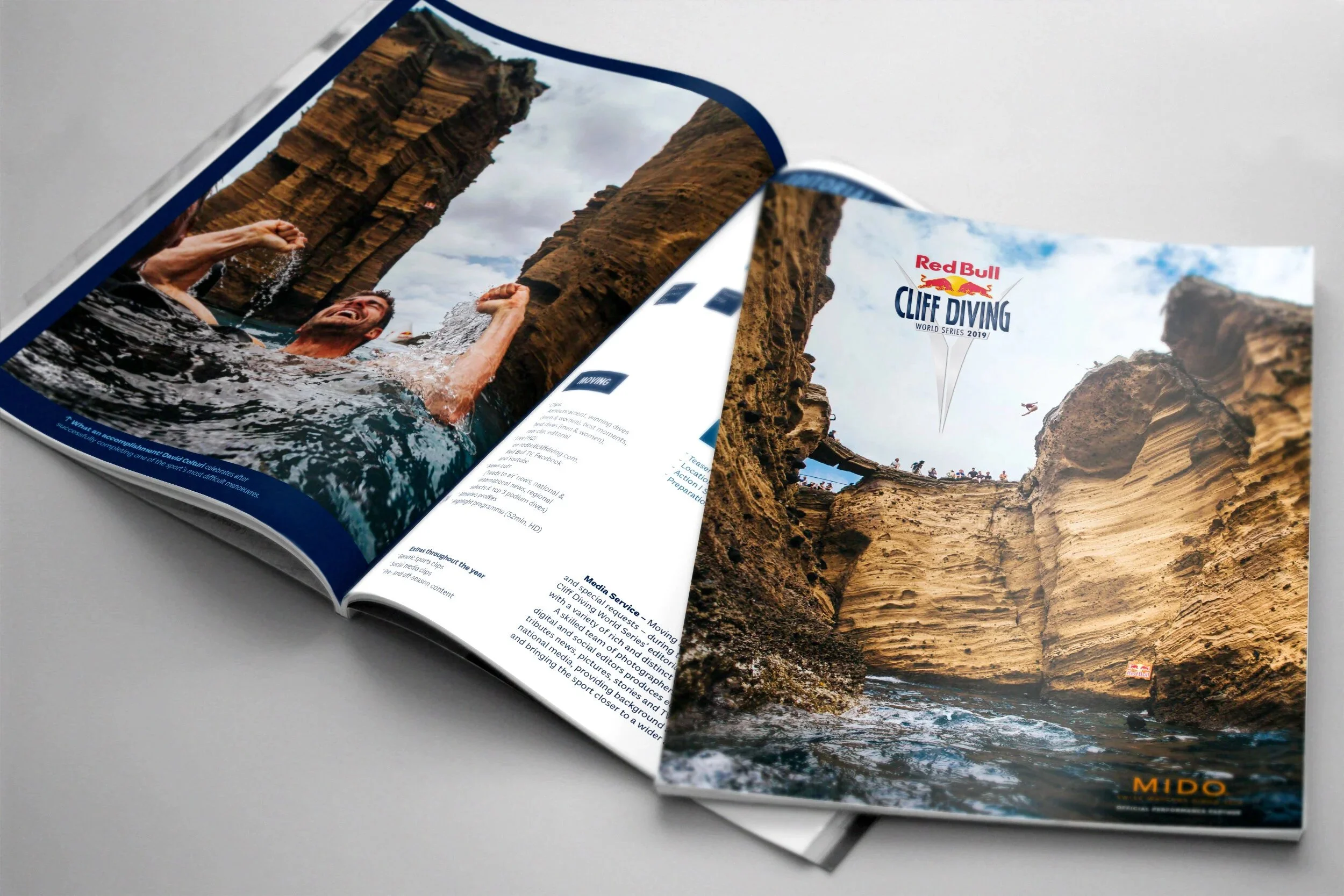Open magazine featuring a poster of cliff diving at Red Bull Cliff Diving World Series 2019, showing a rocky coastal cliff with people watching and a swimmer in the water.