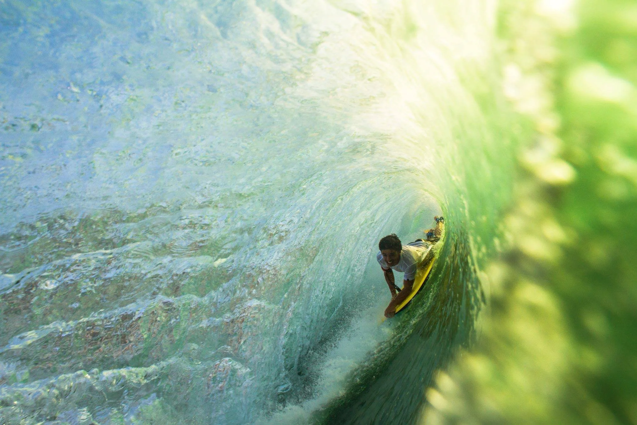 A person surfing inside a large green wave, crouching low on their surfboard, with a smile on their face.