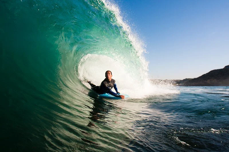 Surfer riding inside a large green wave near the coast on a sunny day.