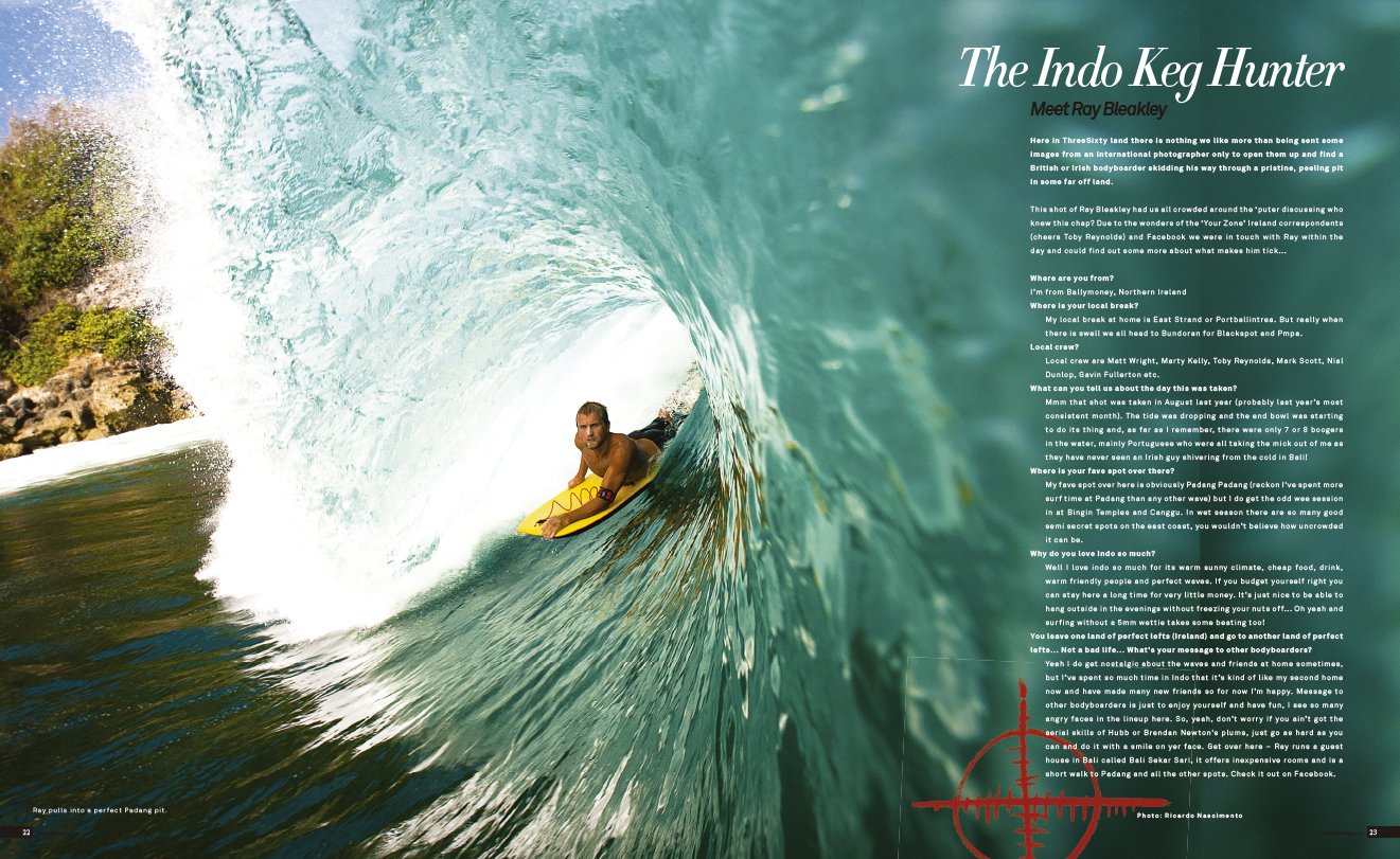 A surfer riding inside a large turquoise wave with sunlight filtering through the water, with rocky shoreline to the left.