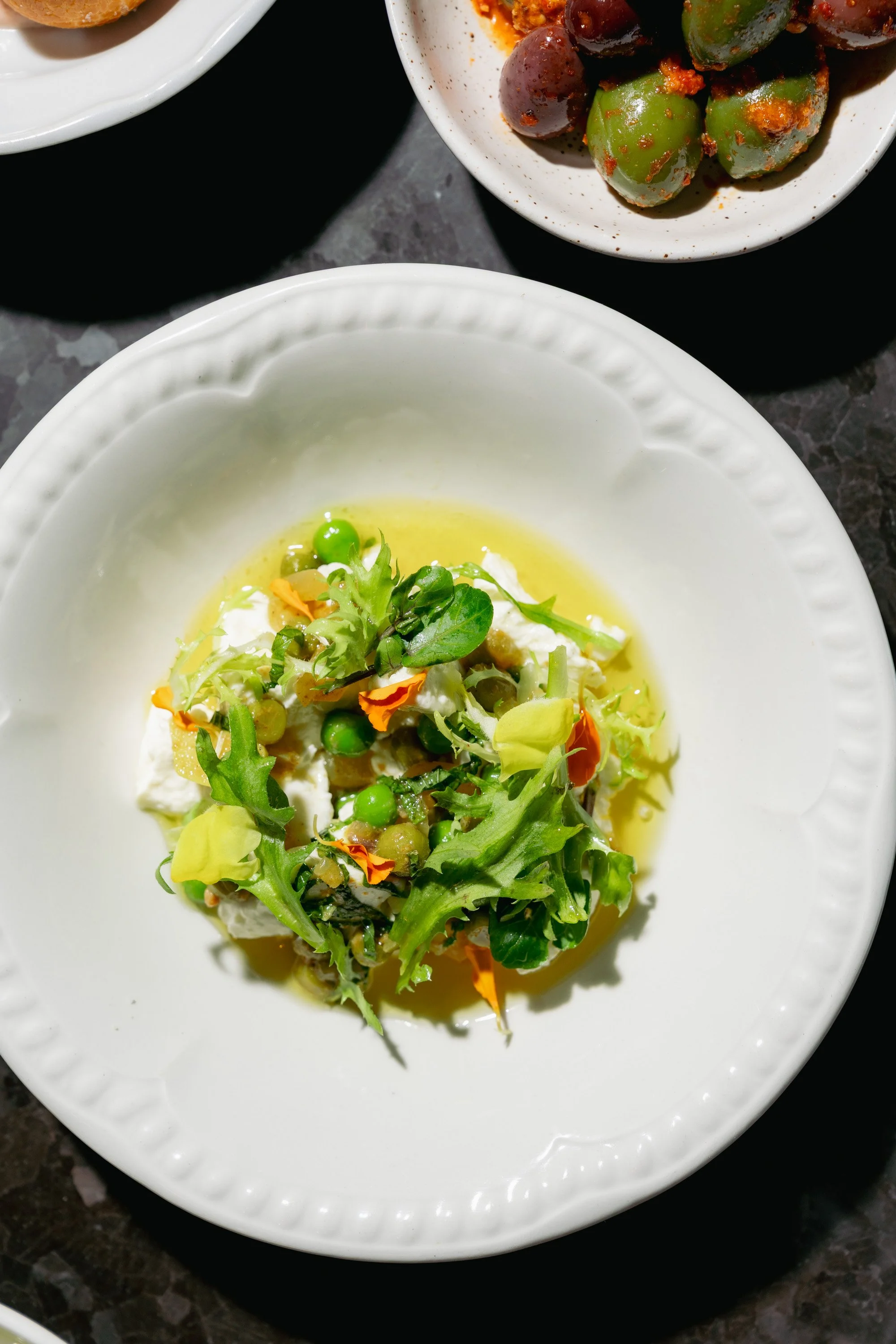A white bowl with a salad of mixed greens, peas, and flower petals in a vinaigrette dressing.
