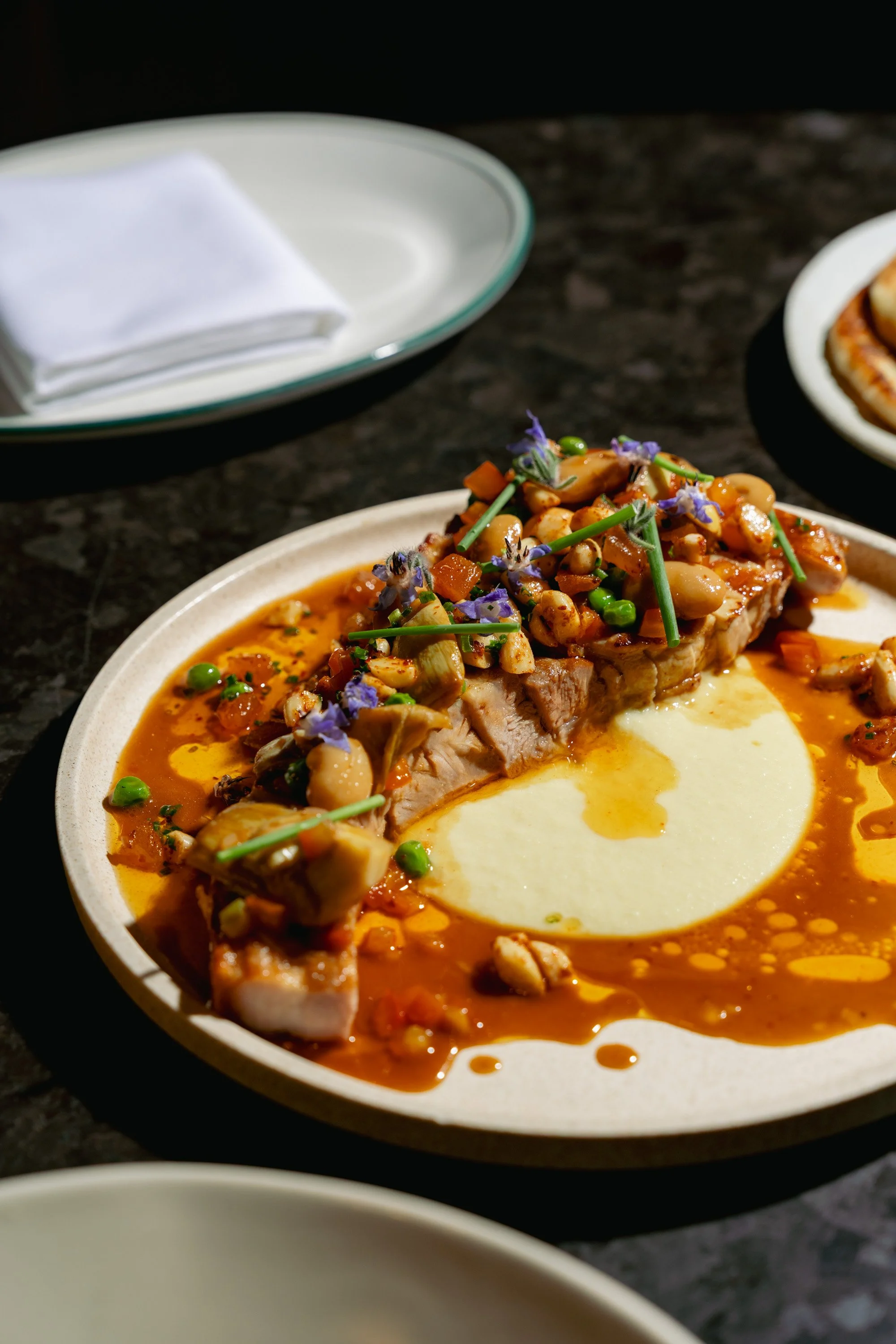 A plate of pork with a vegetable topping on a sauce with mashed potatoes on the side.