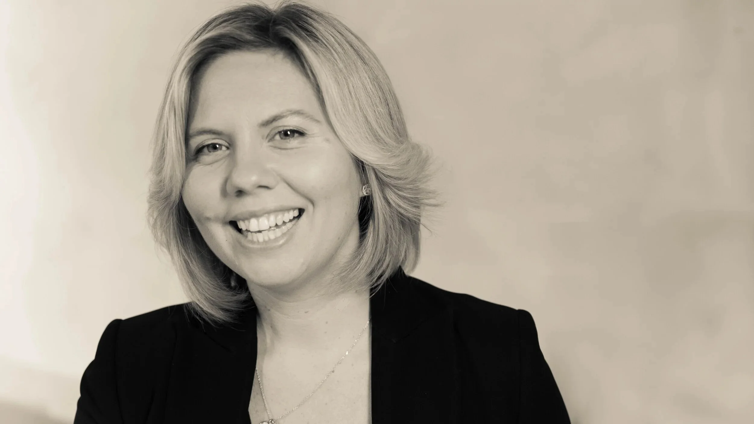 A portrait of a woman with blonde hair, blue eyes, wearing a black blazer, white shirt, smiling, International leadership & executive coach in Paris called Josephine Paris from COACHME ICF PCC coach Bilingual