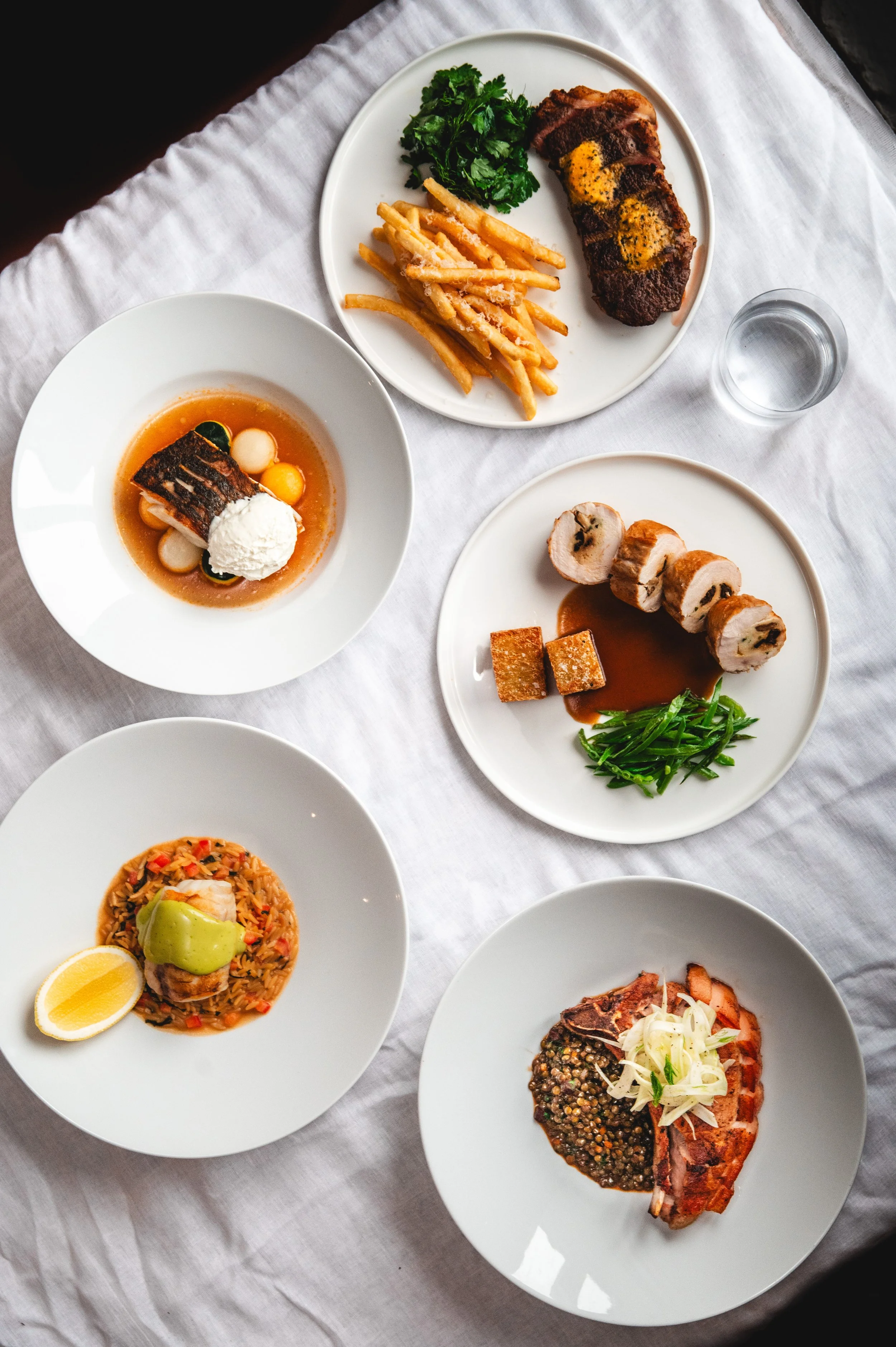 Second from bottom: Plate with rice, grilled chicken, and guacamole; top right: Plate with roast beef, fries, and greens; top left: Bowl with fish, broth, and vegetables; bottom right: Plate with sliced meat, lentil sauce, and onions; center right: P