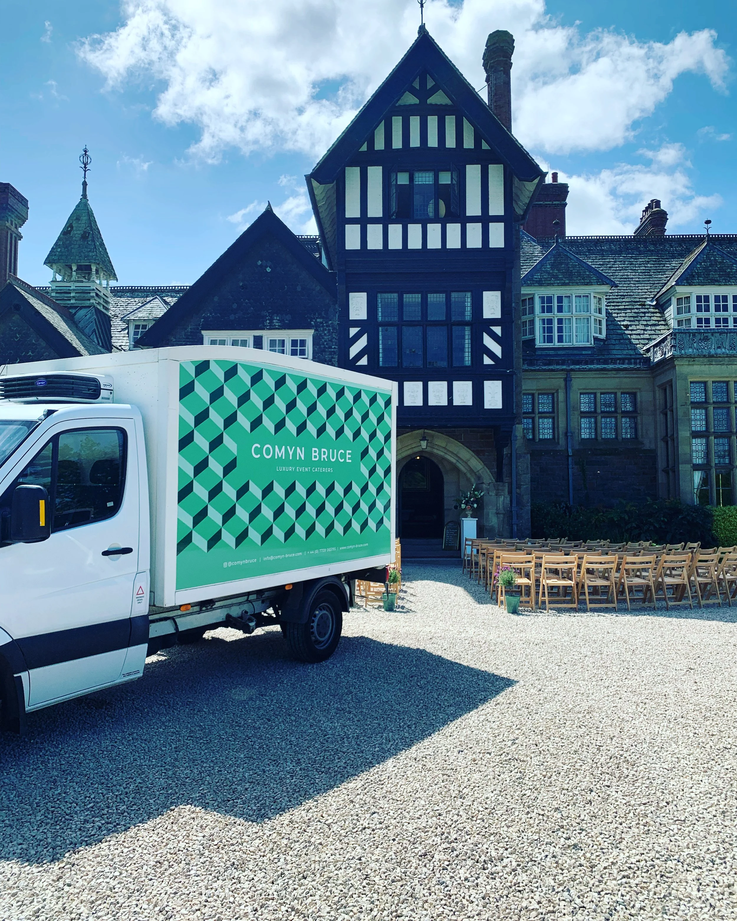 A wedding setup in front of a historic stone building featuring a row of chairs and a truck with branding for Comyn Bruce, a luxury event catering company. Plas Dinam country house, llandinam, wedding catering in mid wales