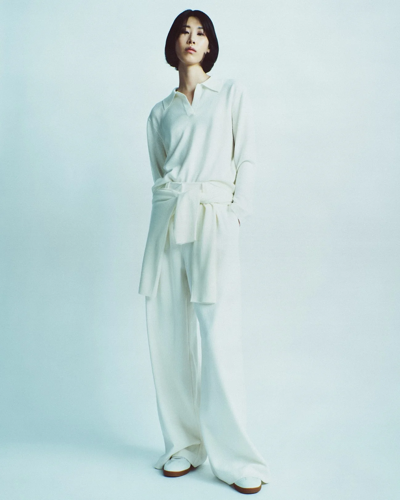 Donna in abito bianco lungo, posa in un ambiente neutro.