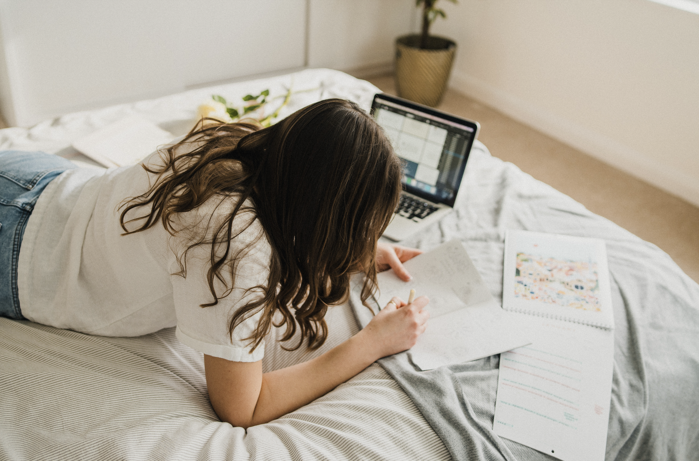 Creative entrepreneur planning a business name with a laptop and notebook on the bed