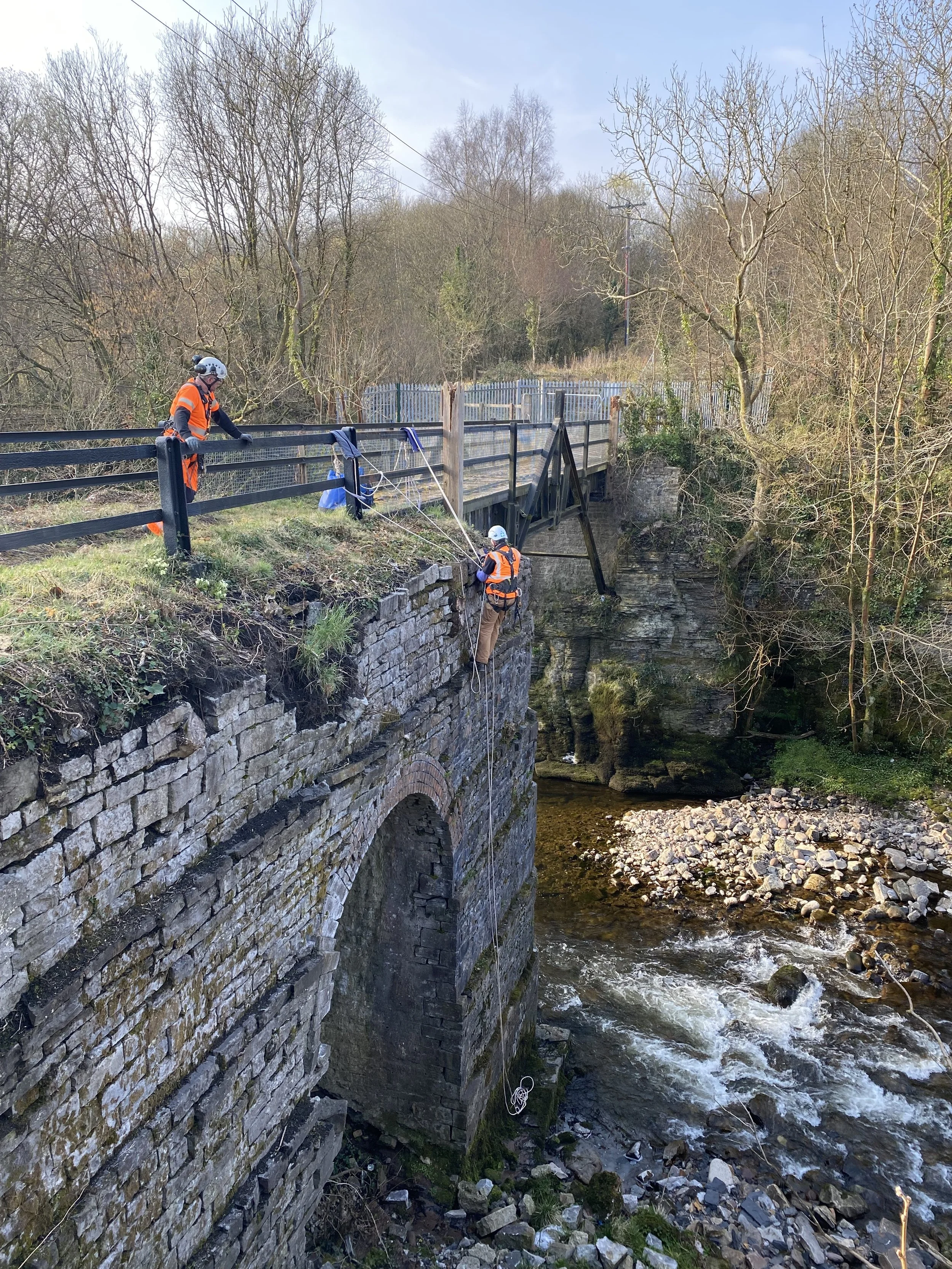 Workers abseiling the side of a stone bridge.