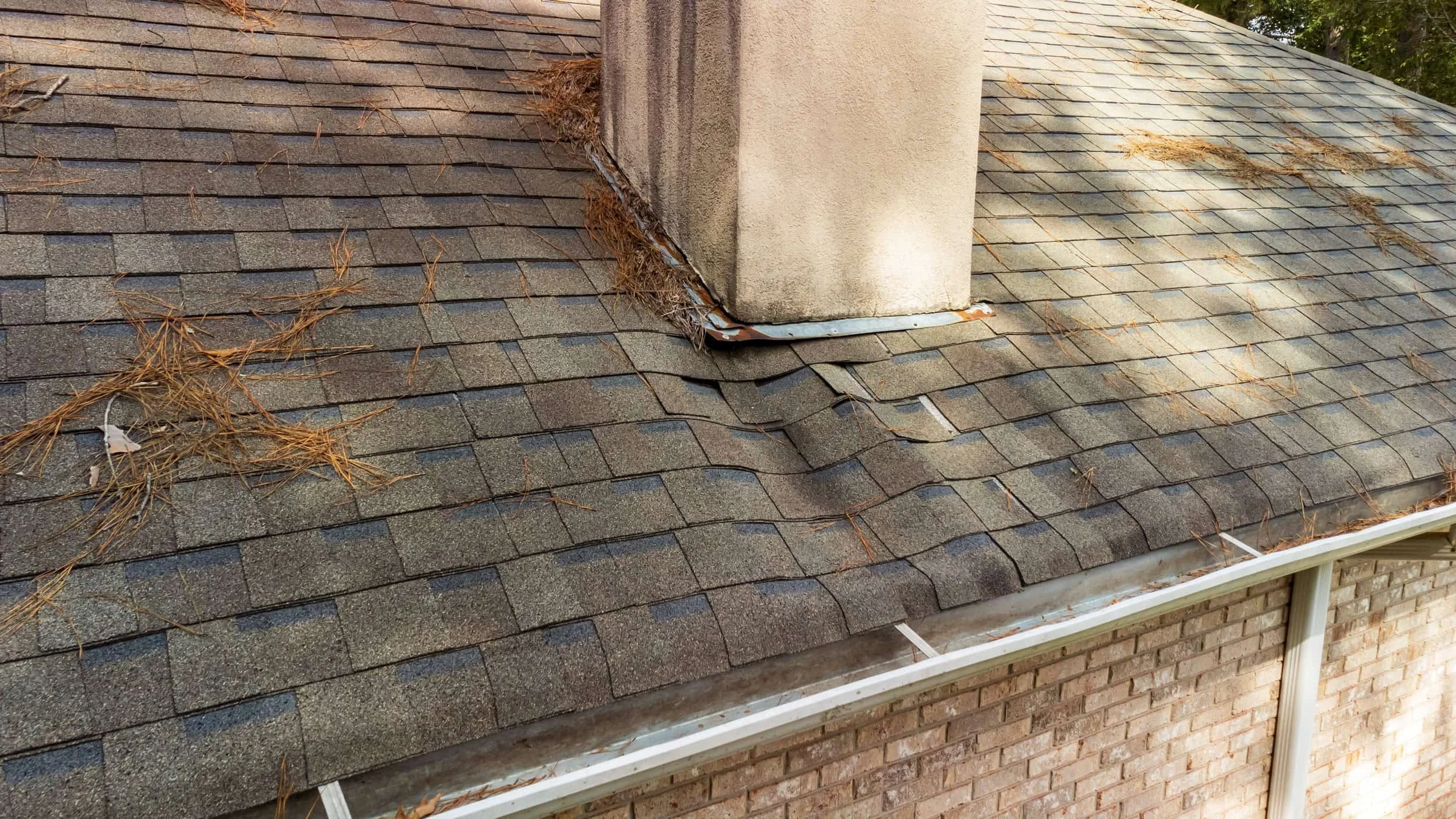 Deteriorating asphalt shingles with buckling and debris around a chimney on a Louisville home