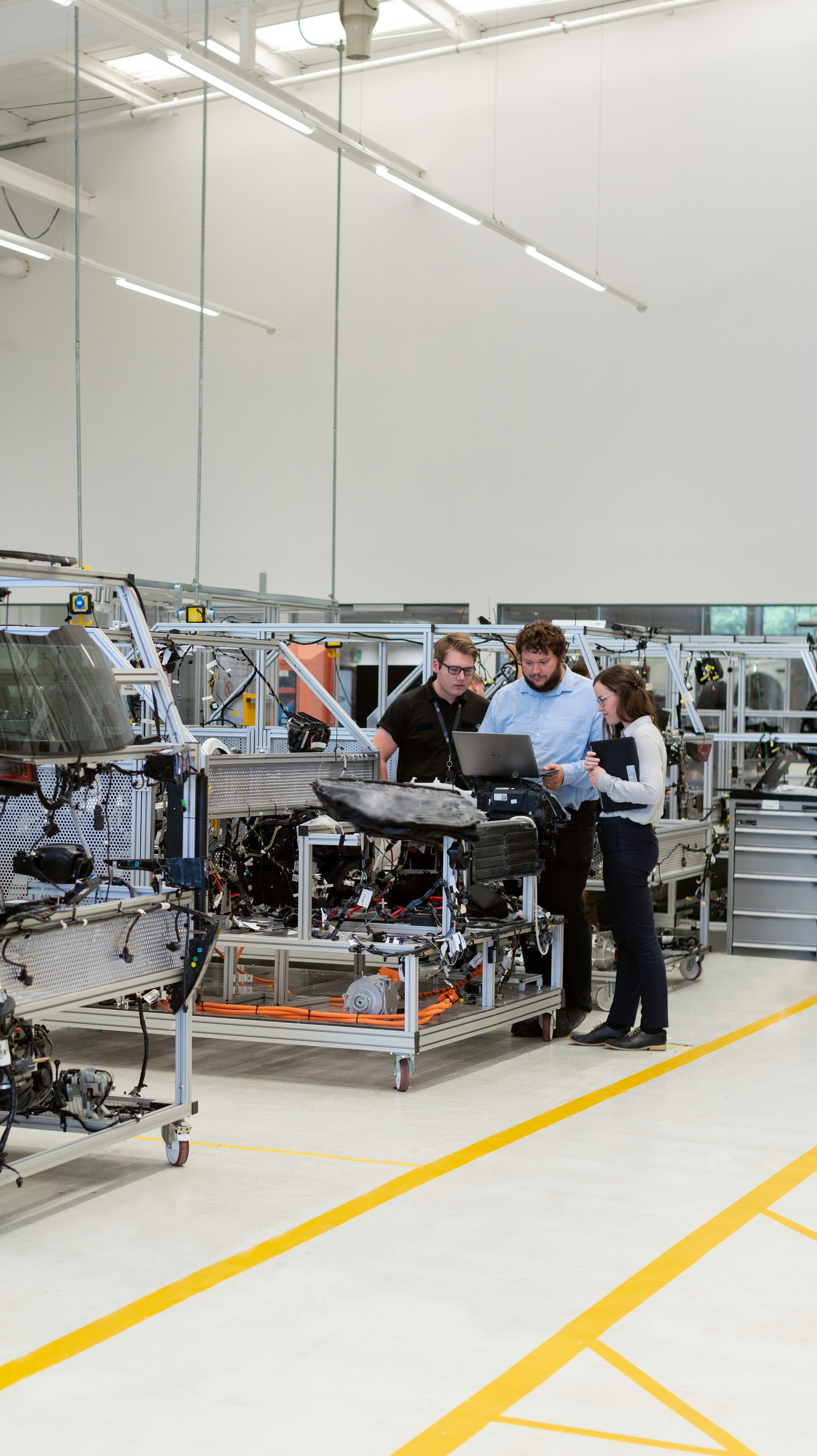 Three engineers examining machinery in a factory or research facility with white walls, high ceilings, and ample lighting.