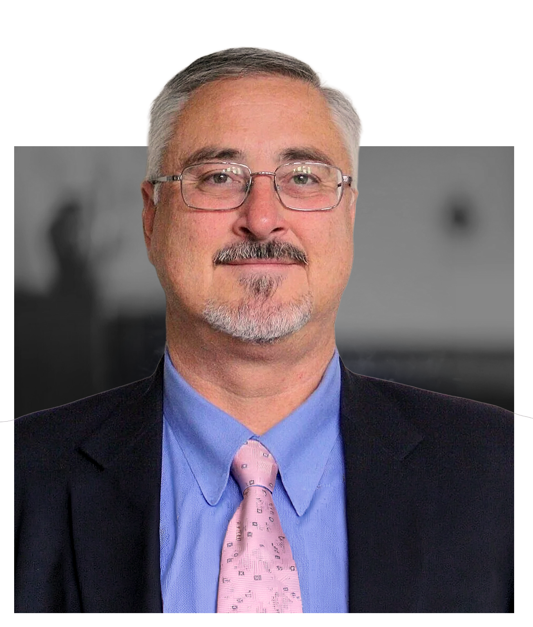 A middle-aged man wearing glasses, a dark suit jacket, a light blue dress shirt, and a pink tie with a subtle pattern, smiling against a blurred background.