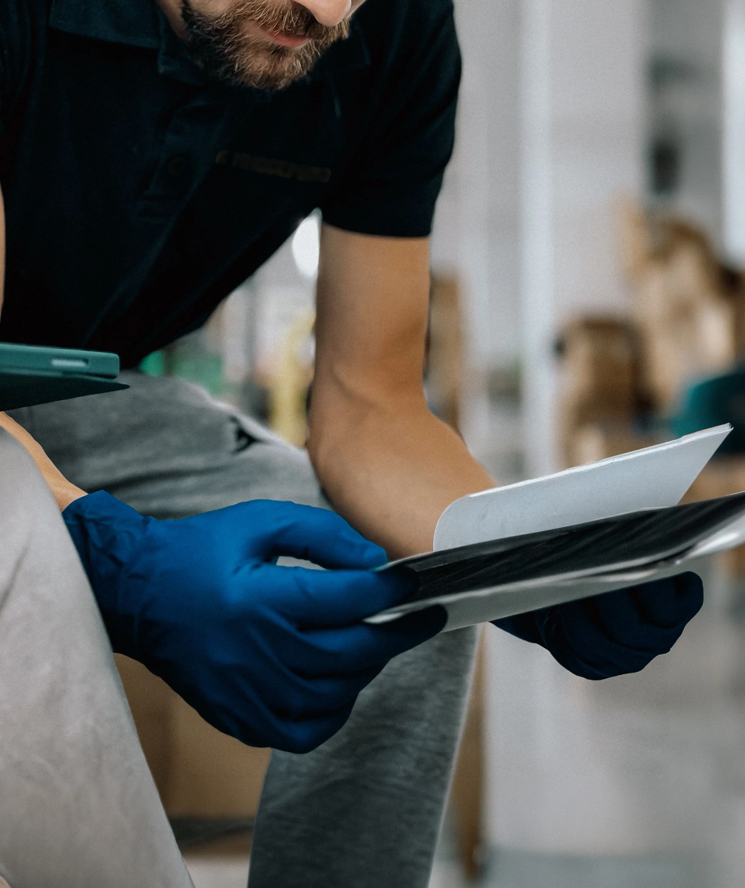 A person wearing black, gray, and blue clothing, with a beard, leaning over and investigating or reading a document and evidence.