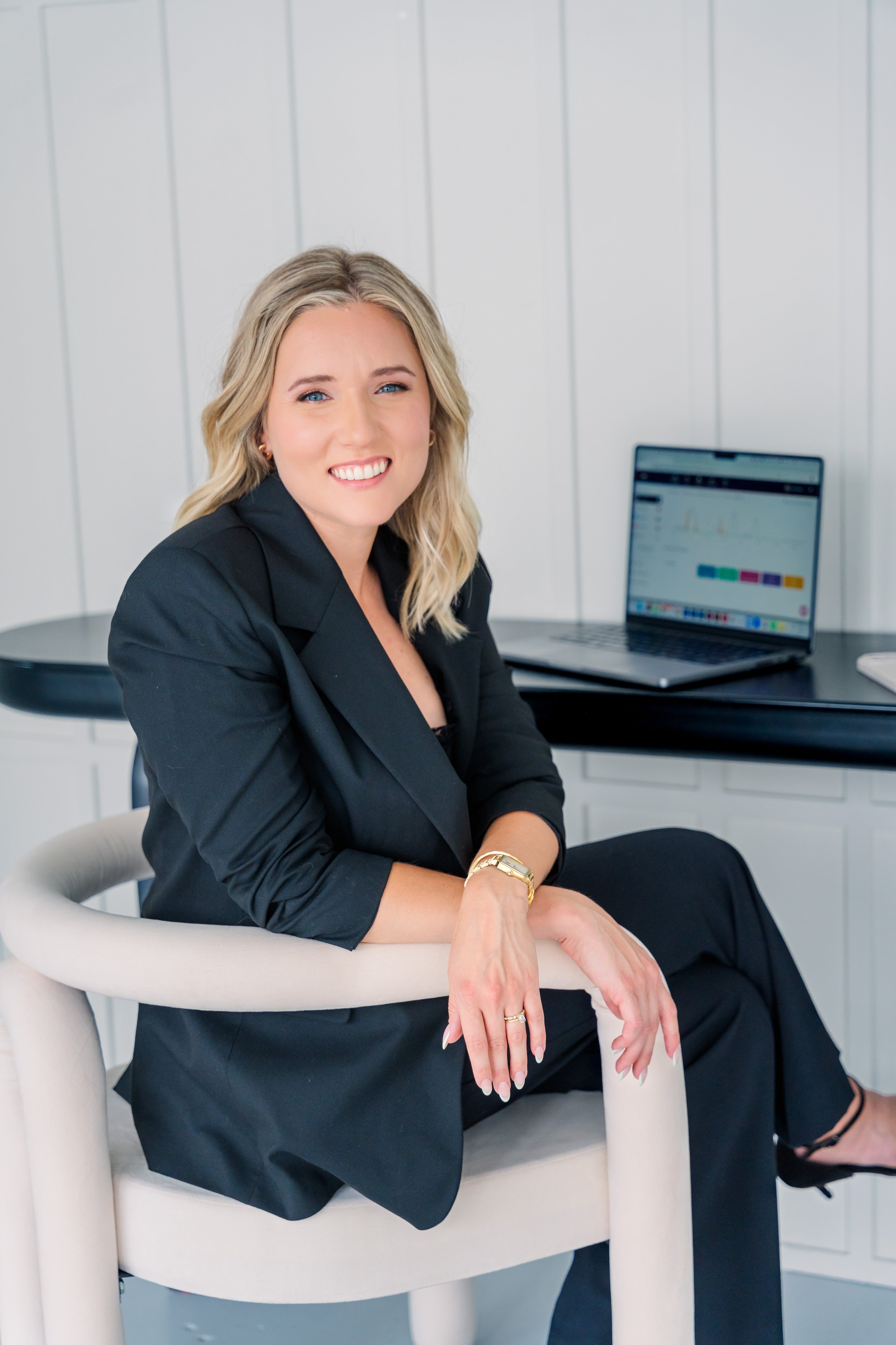 Personal brand photograph of a woman business owner smiling towards the camera with a laptop on a desk in the background