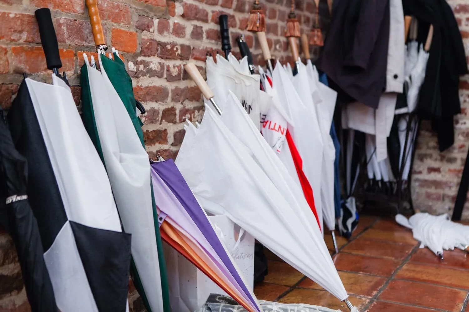 Multiple umbrellas stacked against a brick wall at a wedding.