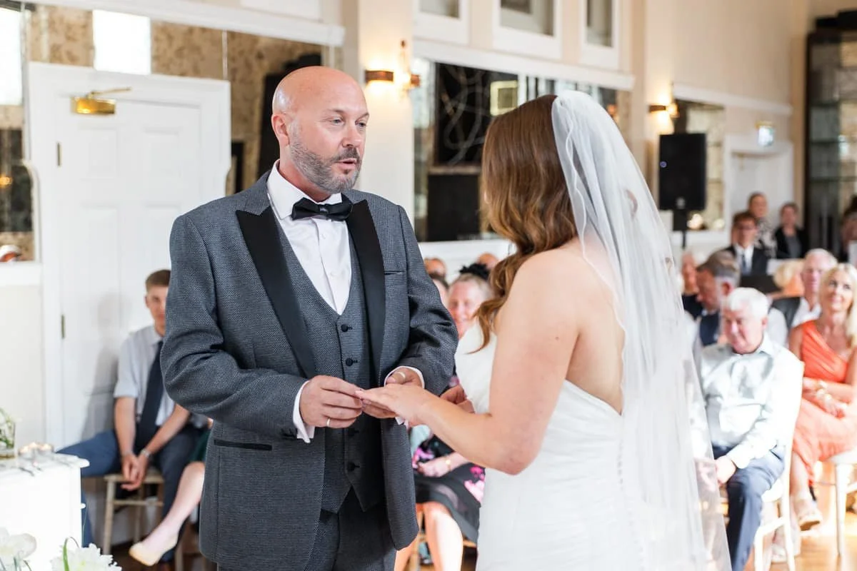 groom holding wedding ring onto bride’s finger
