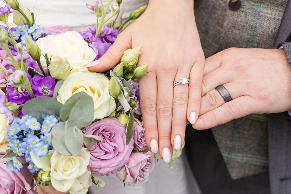 wedding rings on hands next to bouquet