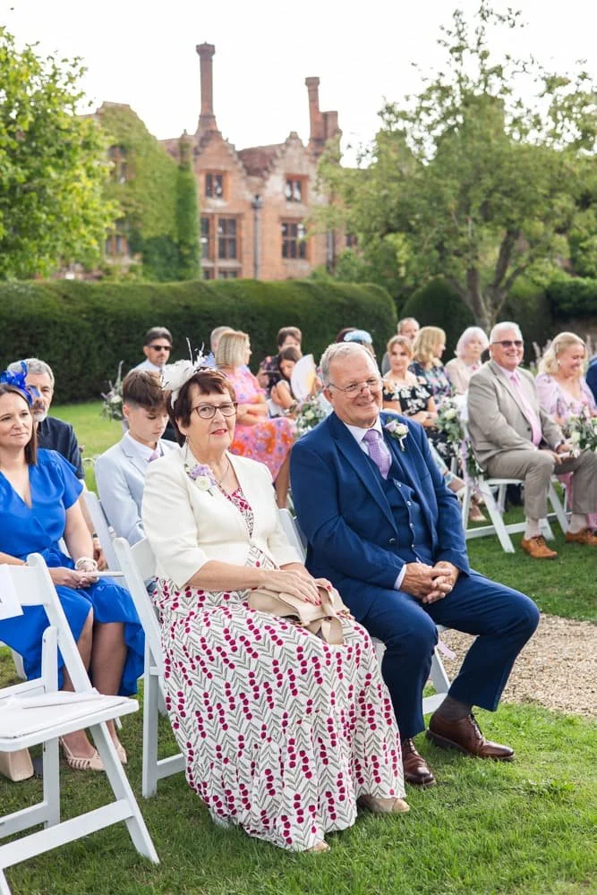 wedding guests seated outside for ceremony with manor house in the background