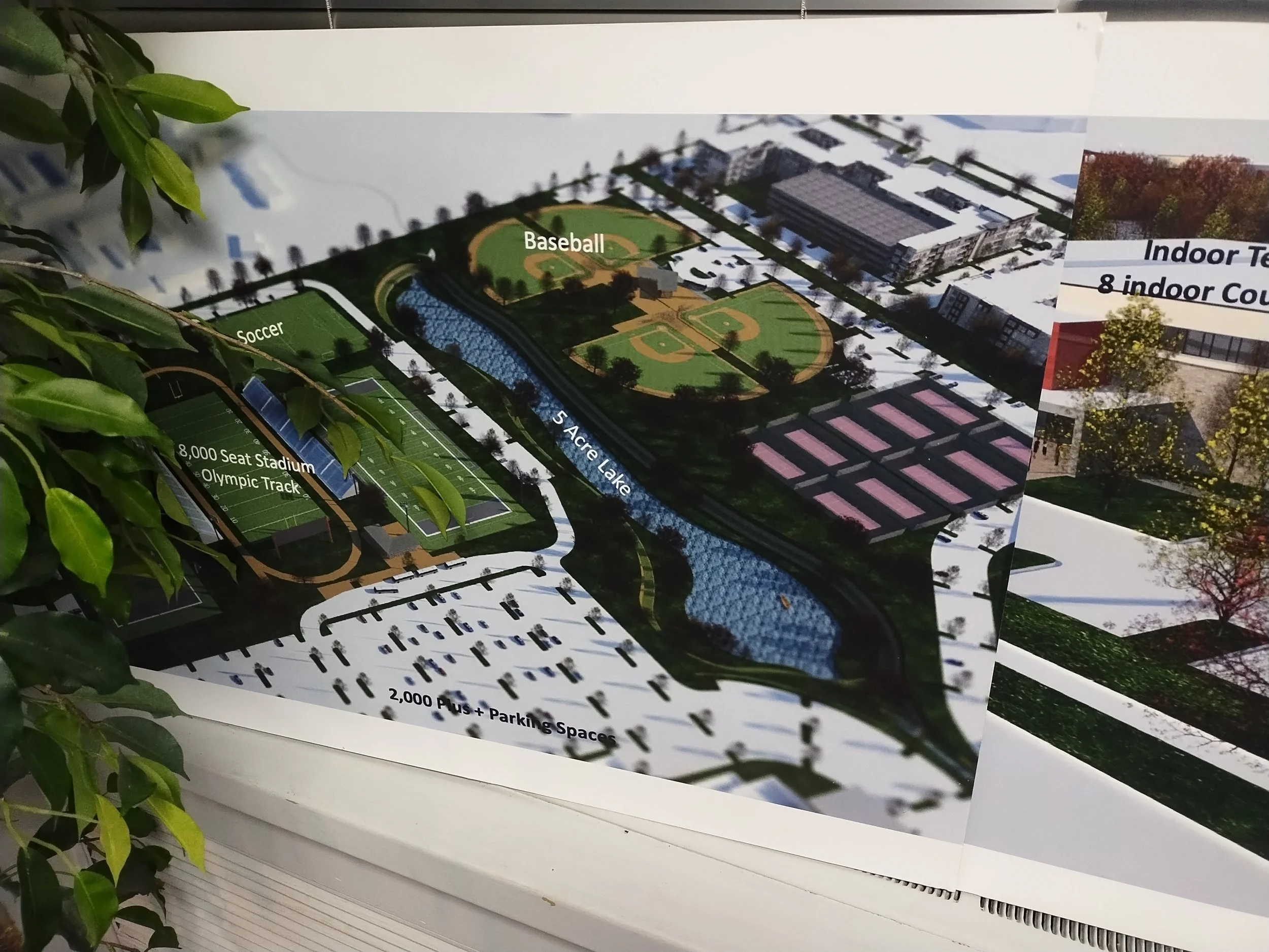 A detailed aerial layout plan of a sports complex showing facilities such as a soccer field, baseball diamond, tennis courts, an Olympic-sized track stadium, a lake, parking lots, and surrounding landscapes.