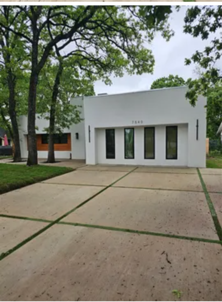 A modern white house with black windows, surrounded by trees and a concrete driveway.