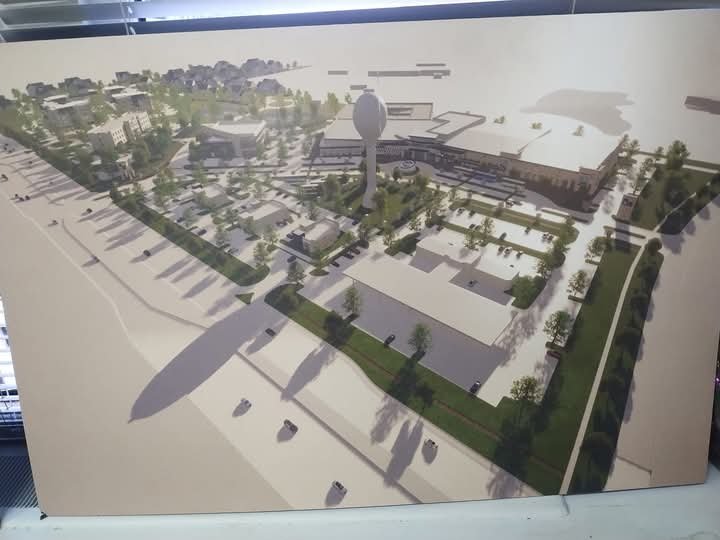 Architectural rendering of a mixed-use development with buildings, green spaces, a water feature, and a central tower.