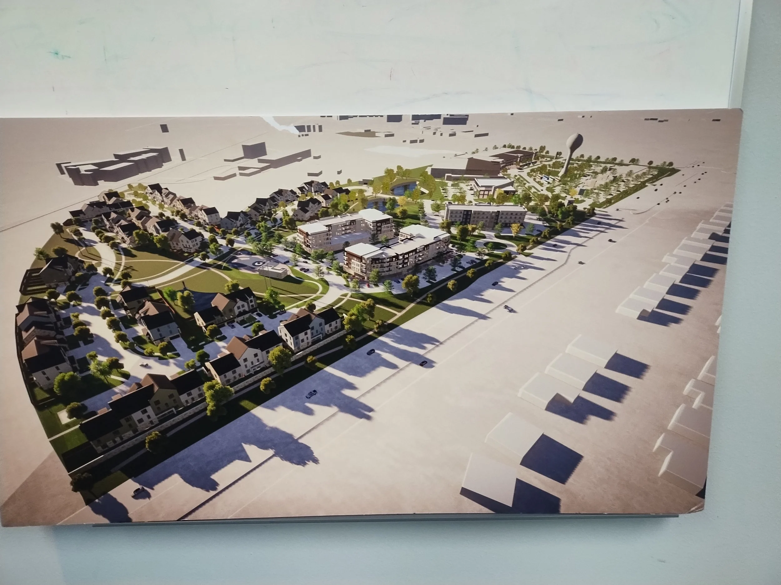 A detailed architectural model of a residential and commercial development with green spaces, pathways, and parking lots.