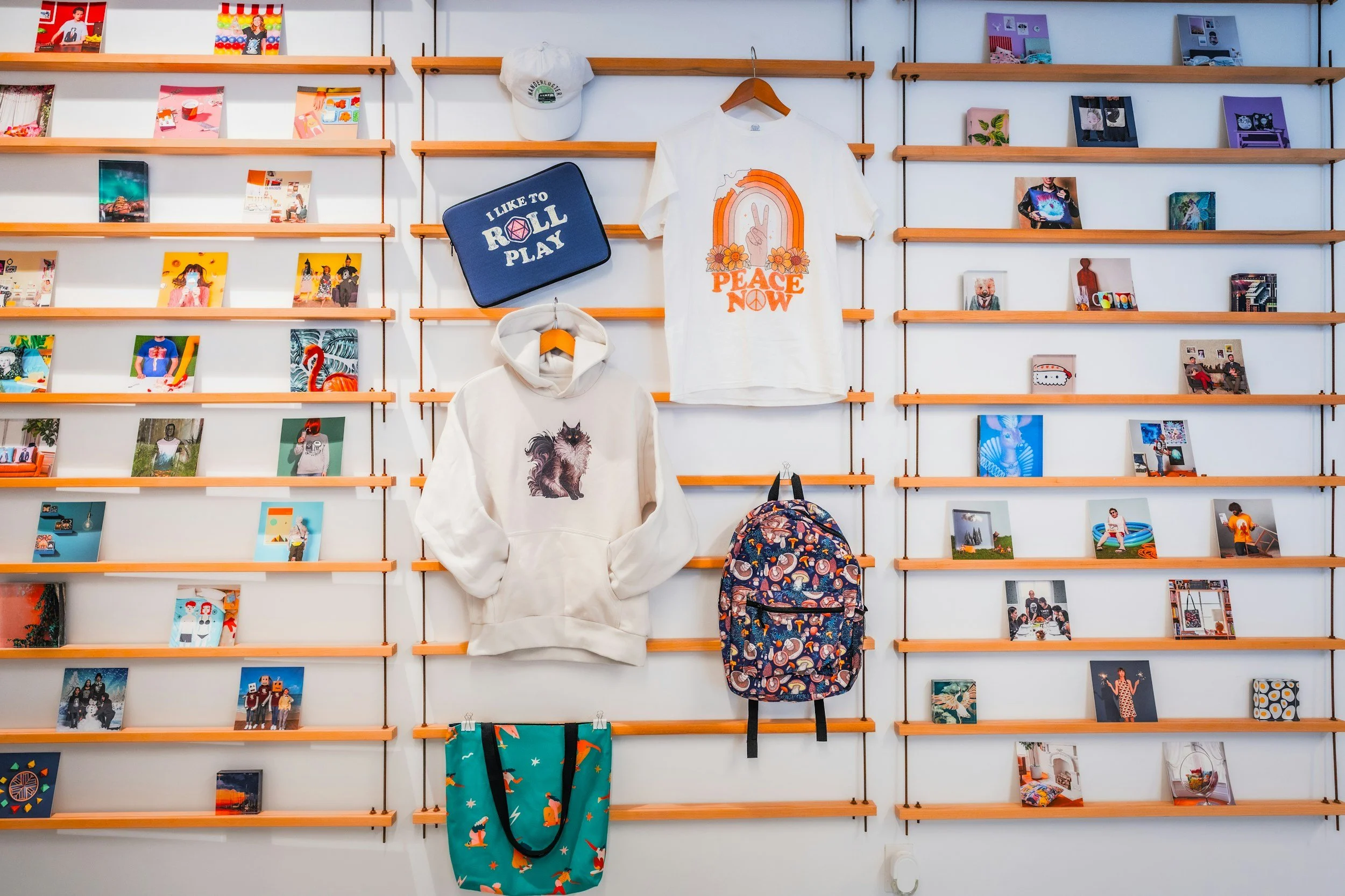 Wall display with small colorful photos, clothing items, and accessories, including hoodies and backpacks, on orange shelves.