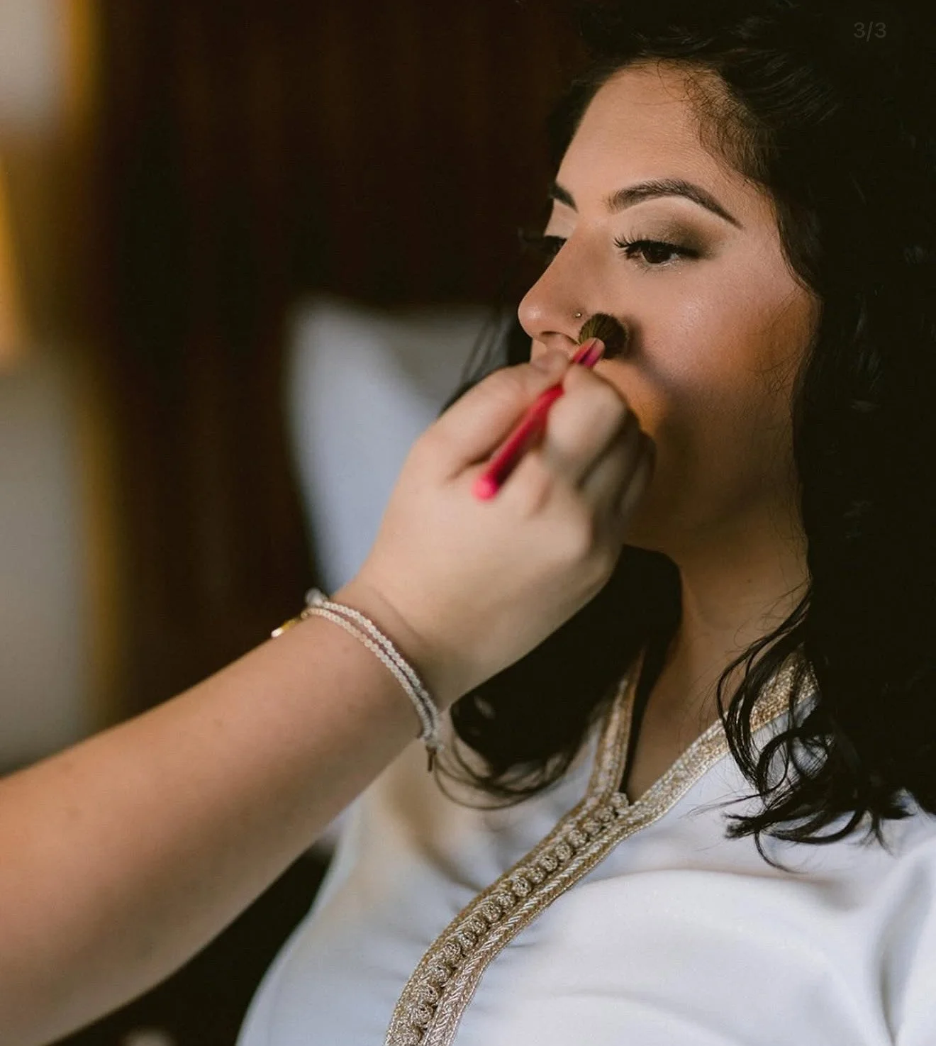 A woman with dark hair and makeup having her face makeup done by a makeup artist using a brush.