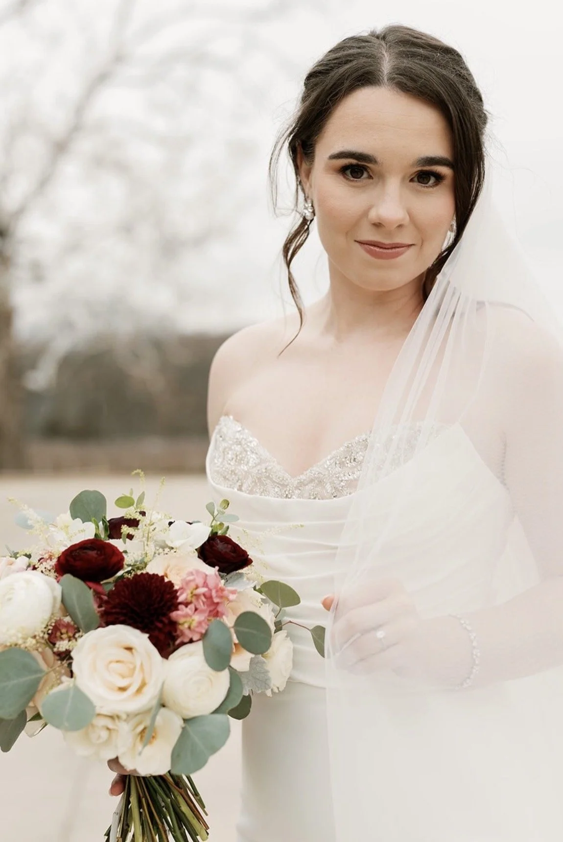 A woman wearing a wedding dress holding a bouquet of flowers at an outdoor setting.