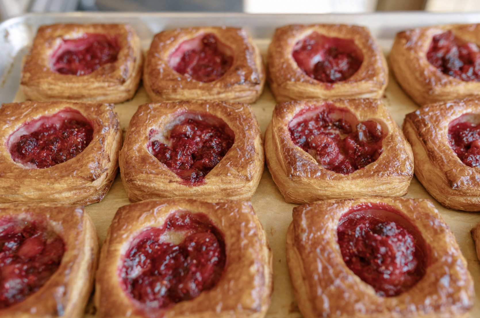 Close-up view of multiple raspberry Danish pastries arranged on a baking tray