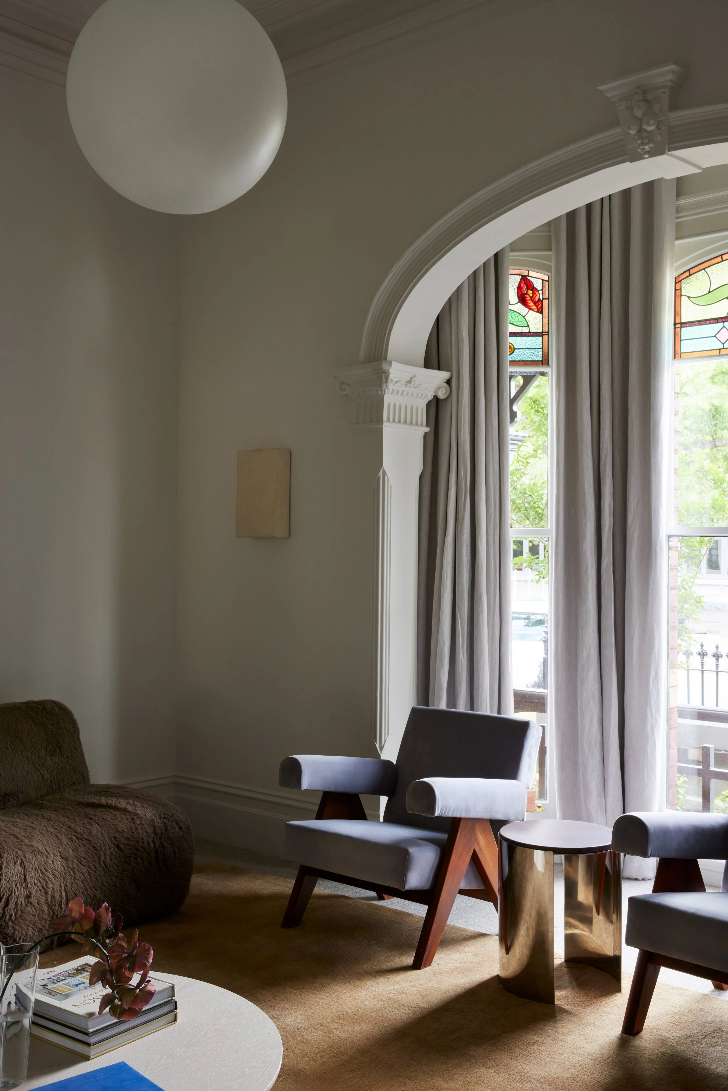Living room with two gray armchairs, a brown sofa, a side table, a plant, and a window with stained glass and curtains.